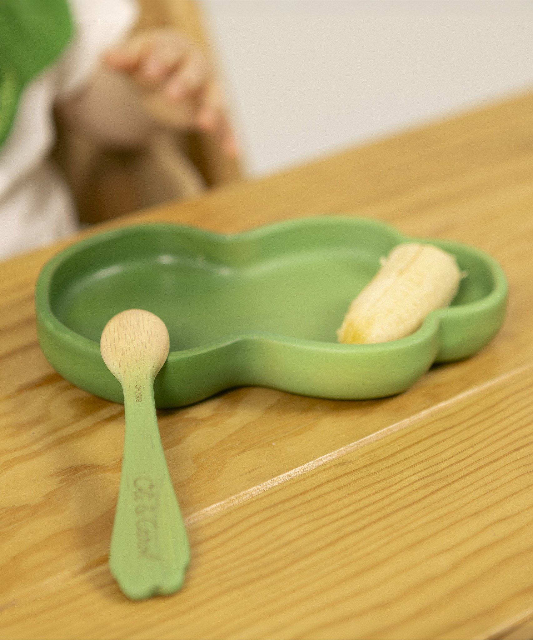 A close up of the Oli & Carol wooden leek spoon from the kale and leek set resting on a kale plate available at Babipur.