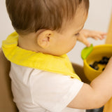 A baby eating fruit and wearing the Oli & Carol Lou the lemon organic cotton baby bib available at Babipur 