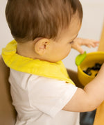 A baby eating fruit and wearing the Oli & Carol Lou the lemon organic cotton baby bib available at Babipur 