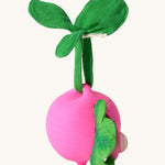 The Ramona Radish Pacifier Holder on a cream background. The image shows an Oli & Carol radish teething toy half way inside the holder. The radish is textured and has a green muslin leaf attachment on the top to tie the holder to a pram handle, high chair etc.