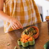 A child standing over the Oli & Carol Cathy the carrot wooden plate and spoon set with food. Set available at Babipur.