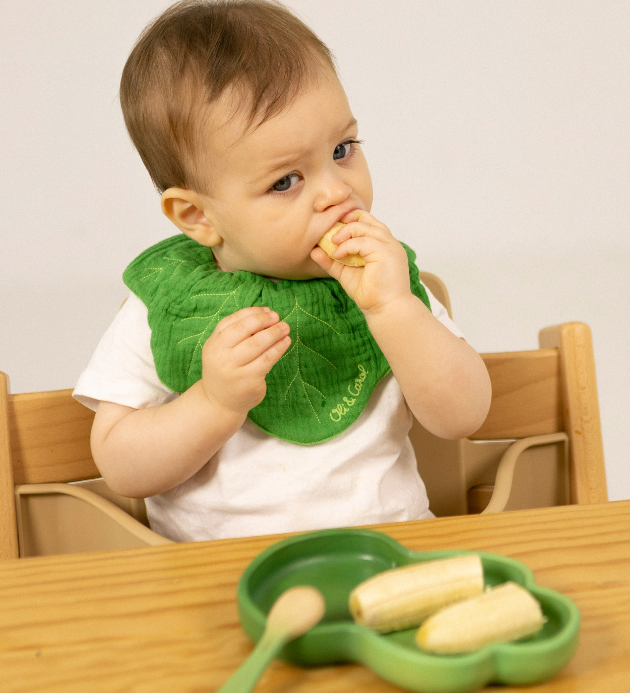 A child eating a banana from the Oli & Carol Kendall the Kale wooden plate and spoon set available at Babipur. 