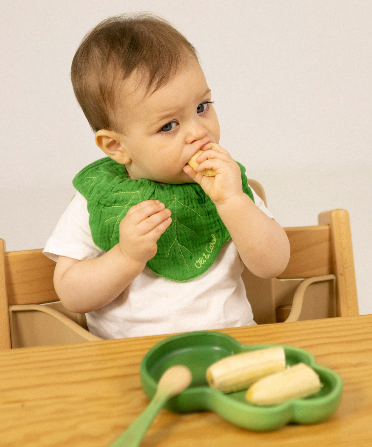 A child eating a banana from the Oli & Carol Kendall the Kale wooden plate and spoon set available at Babipur. 