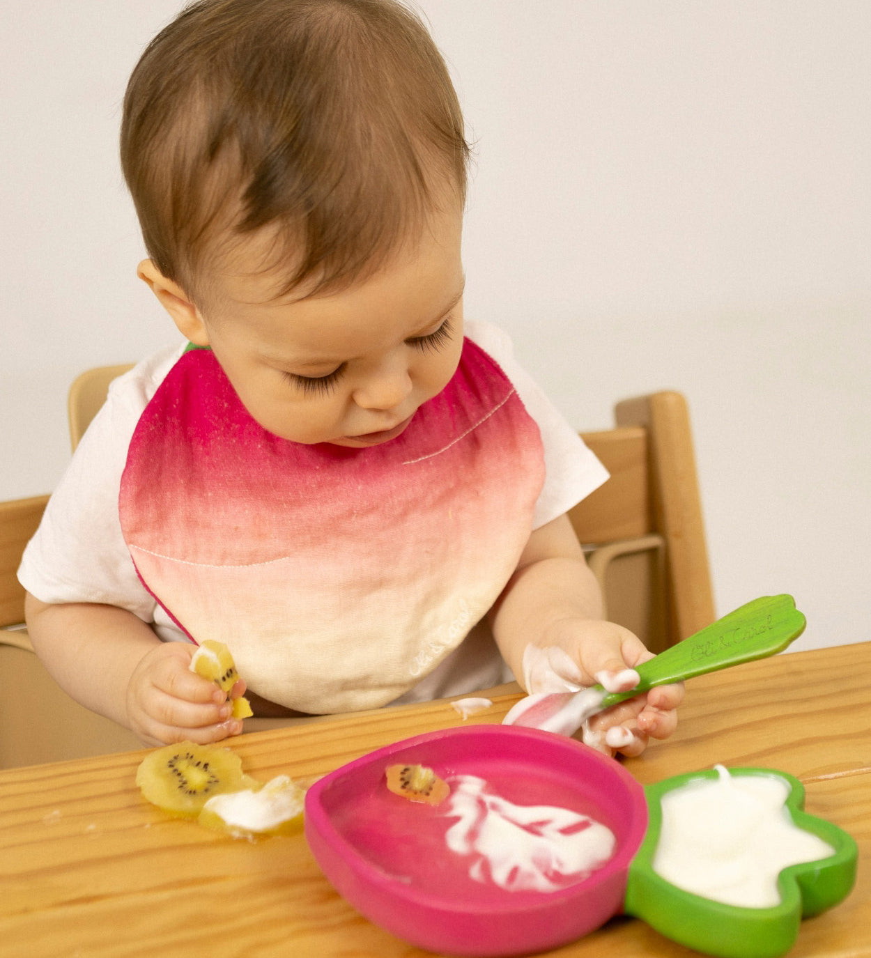 A child eating fruit and yogurt from the Oli & Carol Ramona Radish wooden plate and spoon set available at Babipur. 
