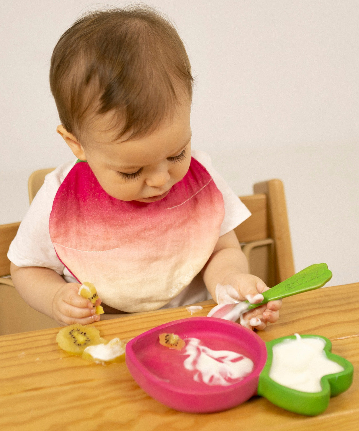 A child eating fruit and yogurt from the Oli & Carol Ramona Radish wooden plate and spoon set available at Babipur. 