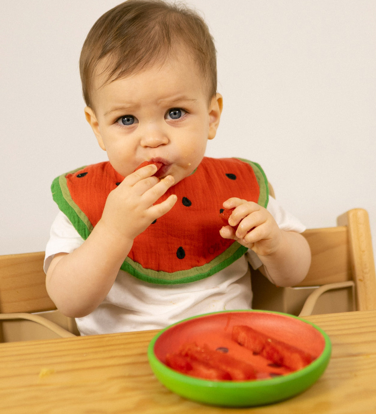 A child eating watermelon from the Oli & Carol Wally the watermelon wooden plate and spoon set available at Babipur. 