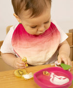 A baby eating fruit and wearing the Oli & Carol Ramona the radish organic cotton baby bib available at Babipur 