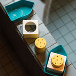 Oli & Carol Boat Bath Toy - Yellow pieces all lined up in a row on the side of a light blue tiled bath