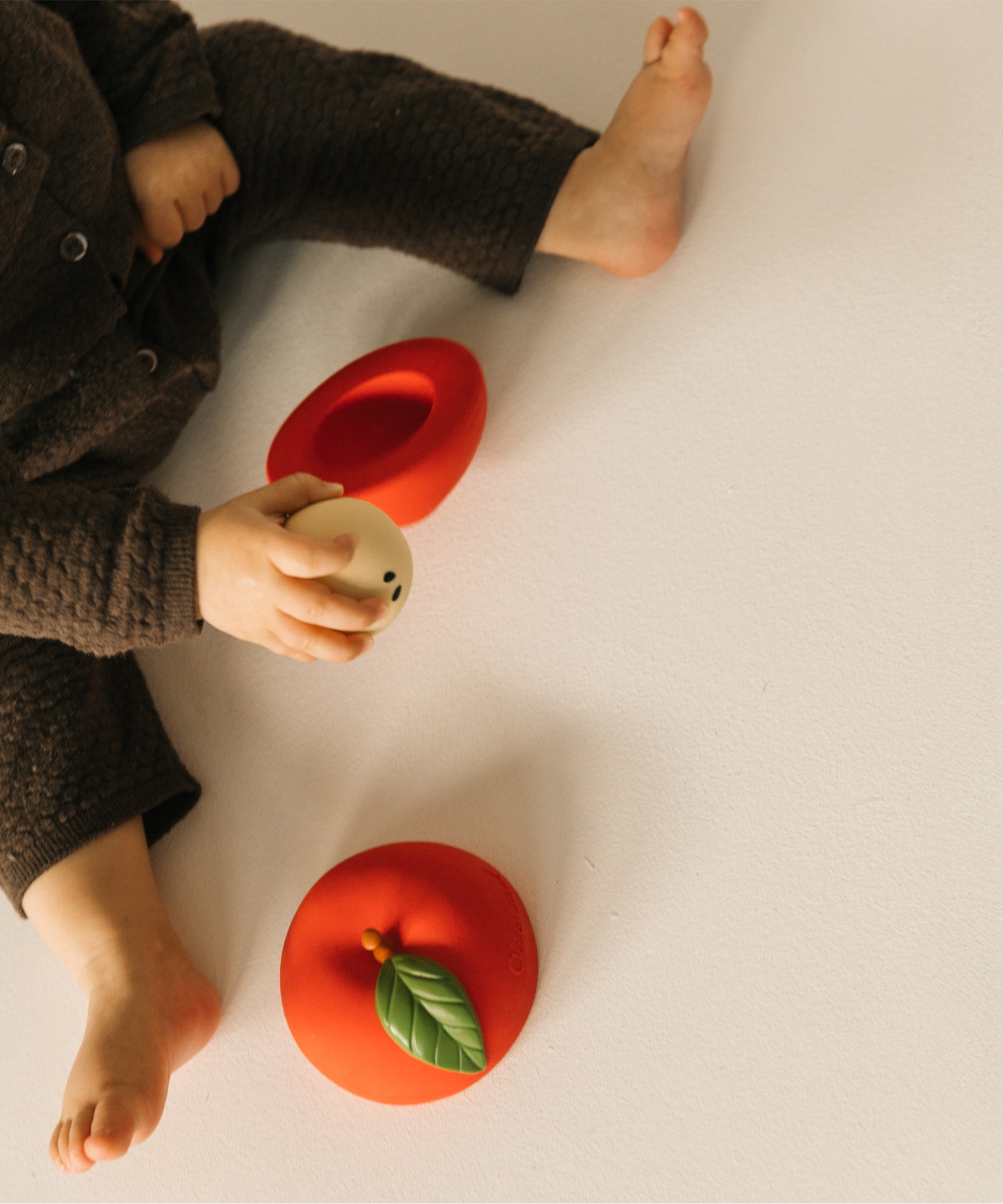 A top down photo of a baby playing with the core from the Oli & Carol red apple stacking toy rattle ball available at Babipur. 