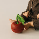 A baby sitting next to the Oli & Carol cherry stacking toy rattle ball available at Babipur.
