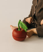 A baby sitting next to the Oli & Carol cherry stacking toy rattle ball available at Babipur.