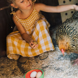 A child sitting with a cockerel with a Oli & Carol Wally the watermelon wooden bowl filled with eggs available at Babipur. 