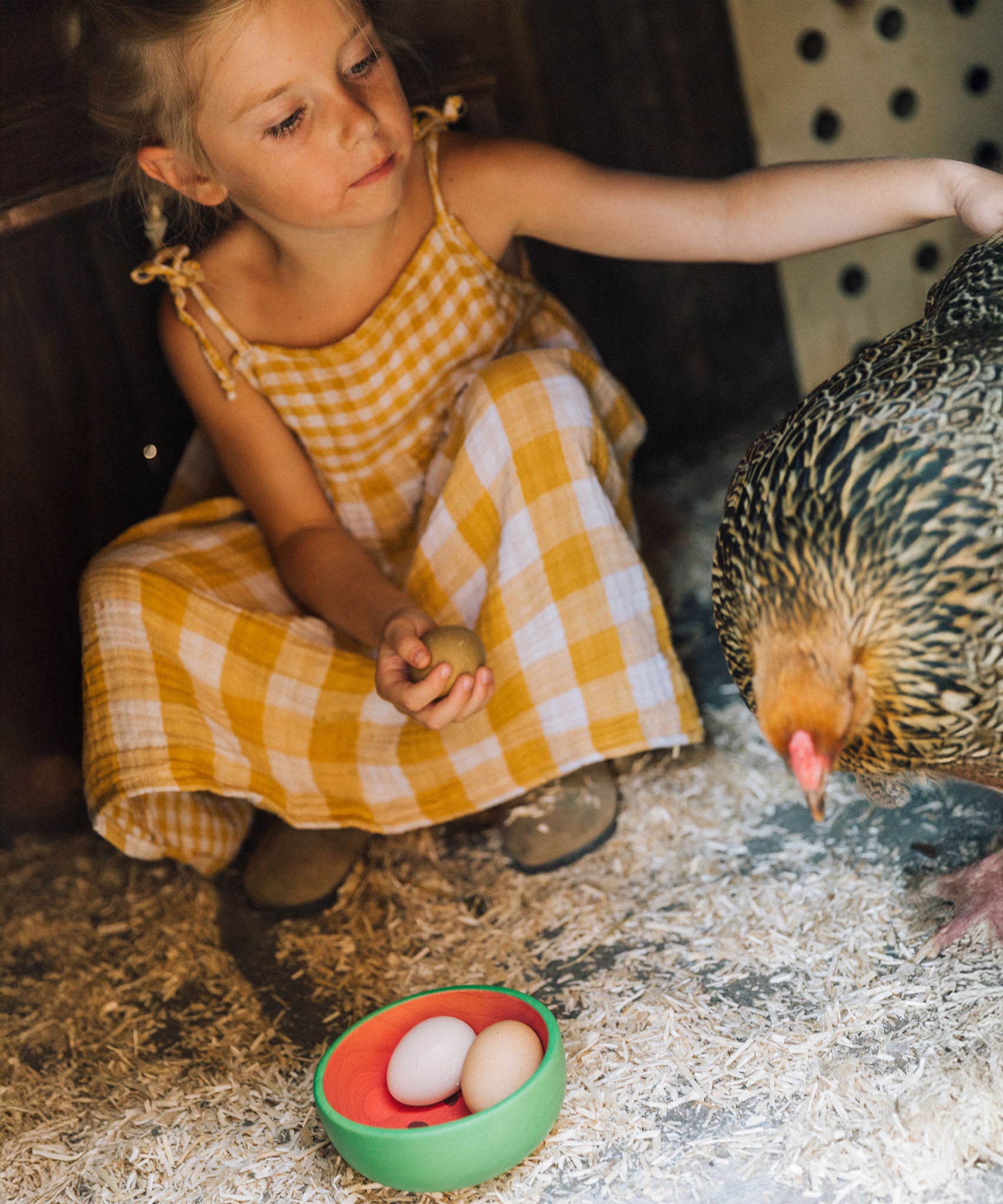 A child sitting with a cockerel with a Oli & Carol Wally the watermelon wooden bowl filled with eggs available at Babipur. 