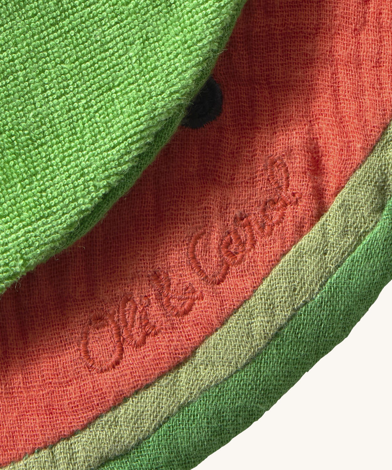 A close up of the  Oli & Carol Wally the watermelon baby bib available at Babipur showing the brand name stitch detail on the inside of the bib