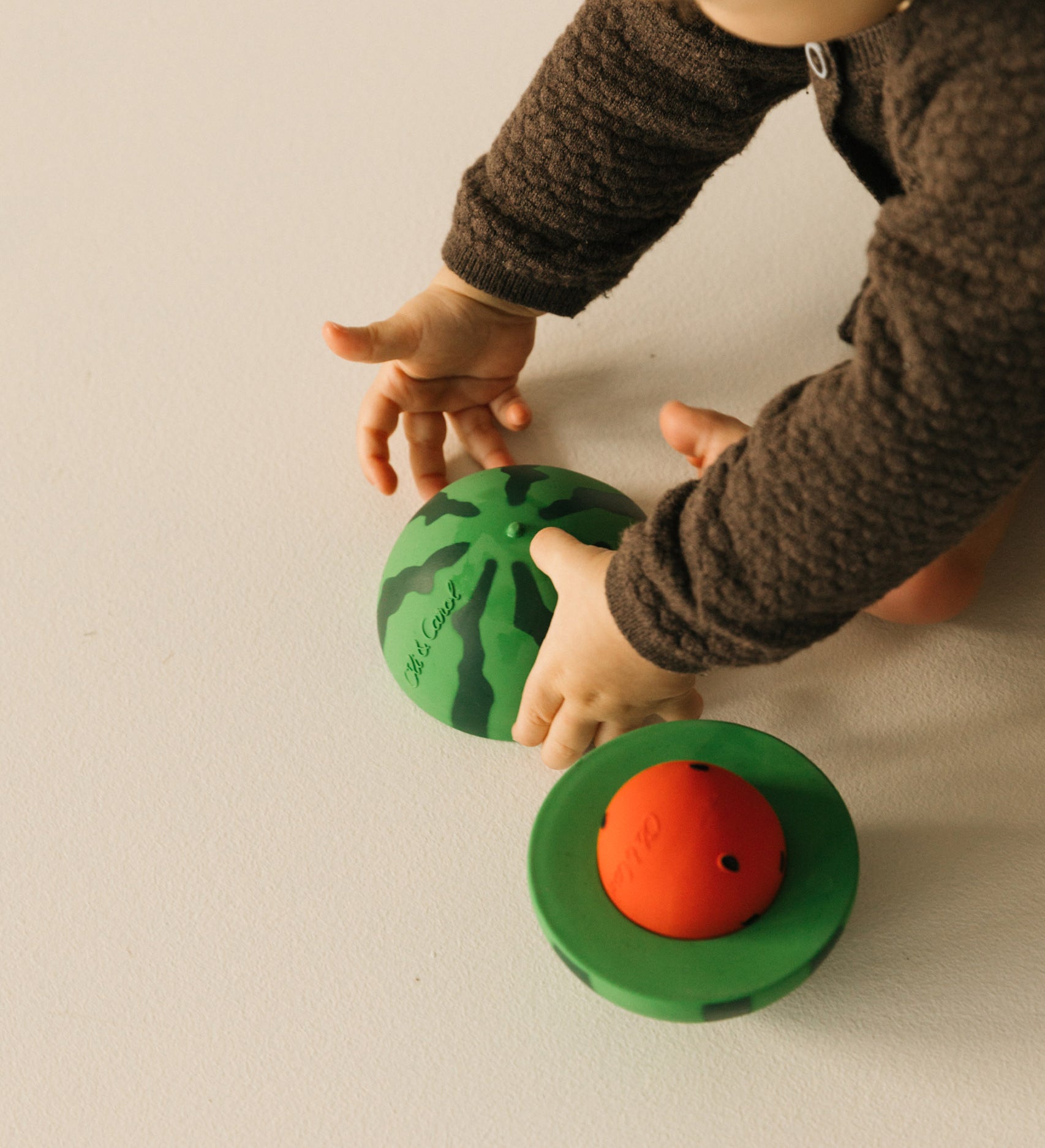 A baby playing with the Oli & Carol watermelon stacking toy rattle ball available at Babipur. 