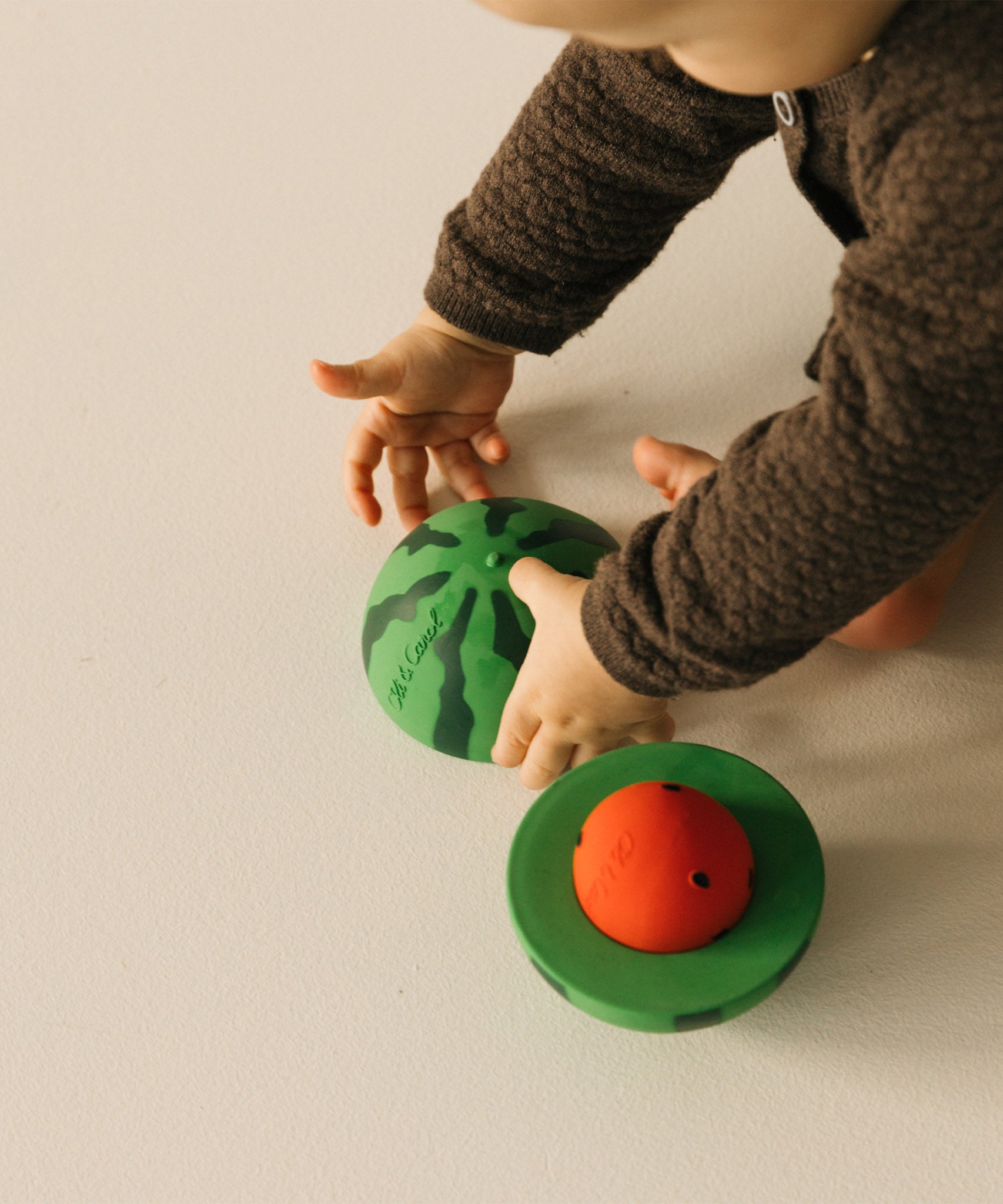 A baby playing with the Oli & Carol watermelon stacking toy rattle ball available at Babipur. 