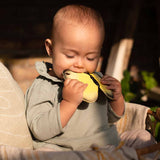 A child sat in the sun, chewing on the Oli & Carol Natural Rubber Teether - Katia The Butterfly