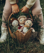 A child is holding the Olli Ella Rattan Poinsettia basket by the handle, in their hands. The basket is on a grassy floor with Christmas Dinky Dinkums inside, and small pine tree branches to give a festive feel.