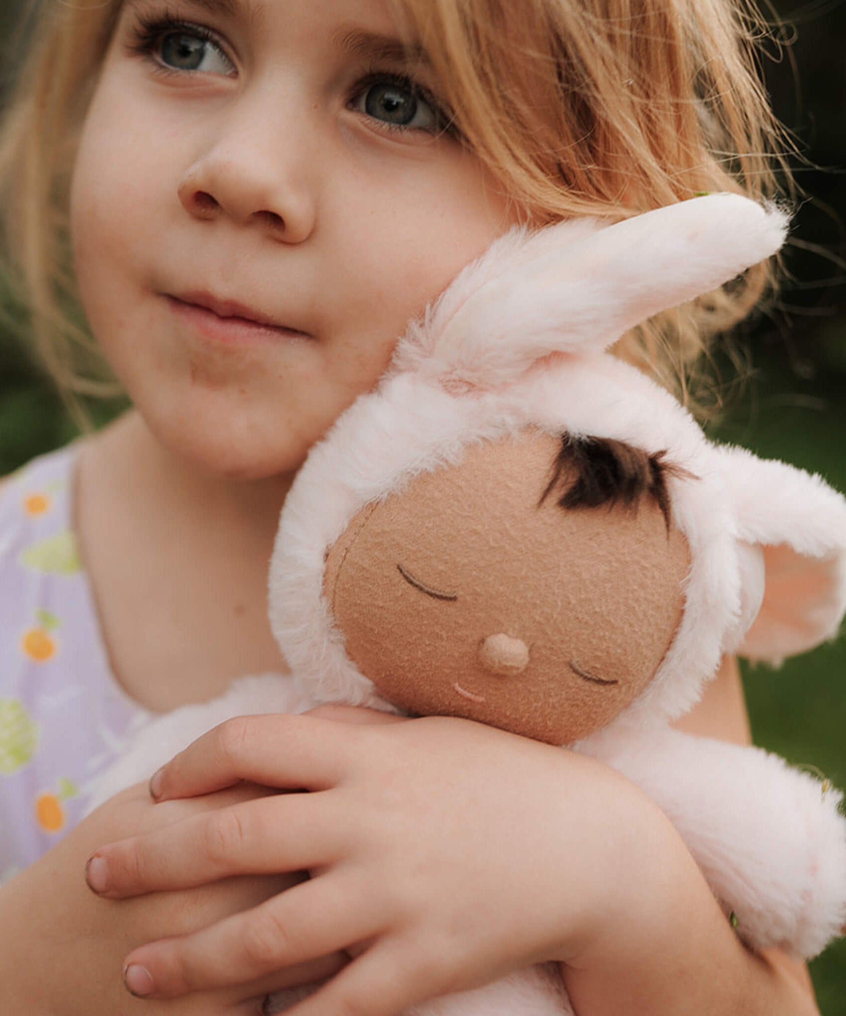 A close up of a girl holding the Olli Ella cozy dinkum bunny pip doll in pink showing the cute sleeping facial features. This fluffy toy doll is available at Babipur.