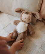 A child tucking a Olli Ella cozy dinkum dog Digby doll in bed. This cosy and fluffy toy doll has a sleeping face, cute floppy ears and available at Babipur