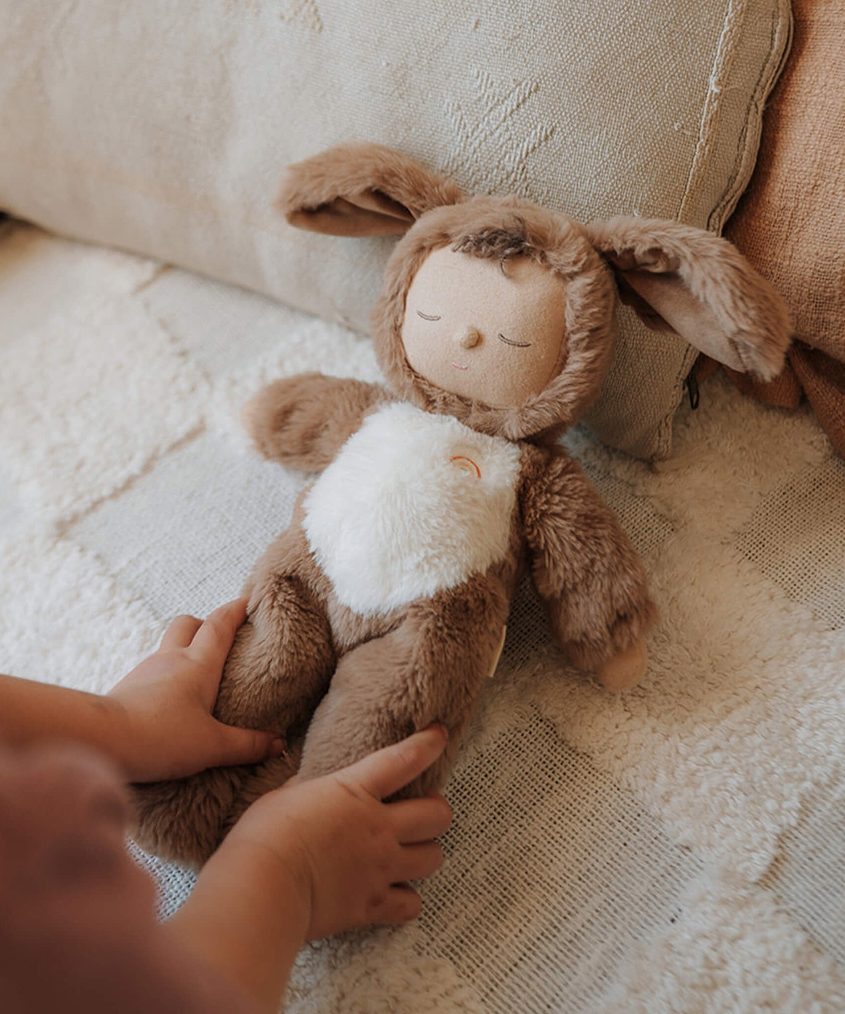 A child tucking a Olli Ella cozy dinkum dog Digby doll in bed. This cosy and fluffy toy doll has a sleeping face, cute floppy ears and available at Babipur