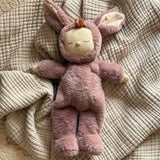 Olli Ella cozy dinkum bunny pickle doll in mauve colour lying on top of a soft blanket. This fluffy toy is available at Babipur