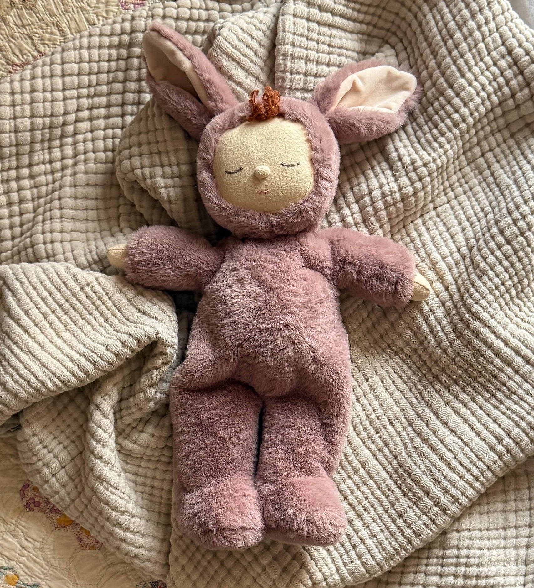 Olli Ella cozy dinkum bunny pickle doll in mauve colour lying on top of a soft blanket. This fluffy toy is available at Babipur