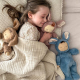 A girl sleeping next to Olli Ella cozy dinkum bunnies including the blue twiggy bunny. These fluffy toy dolls are available at Babipur