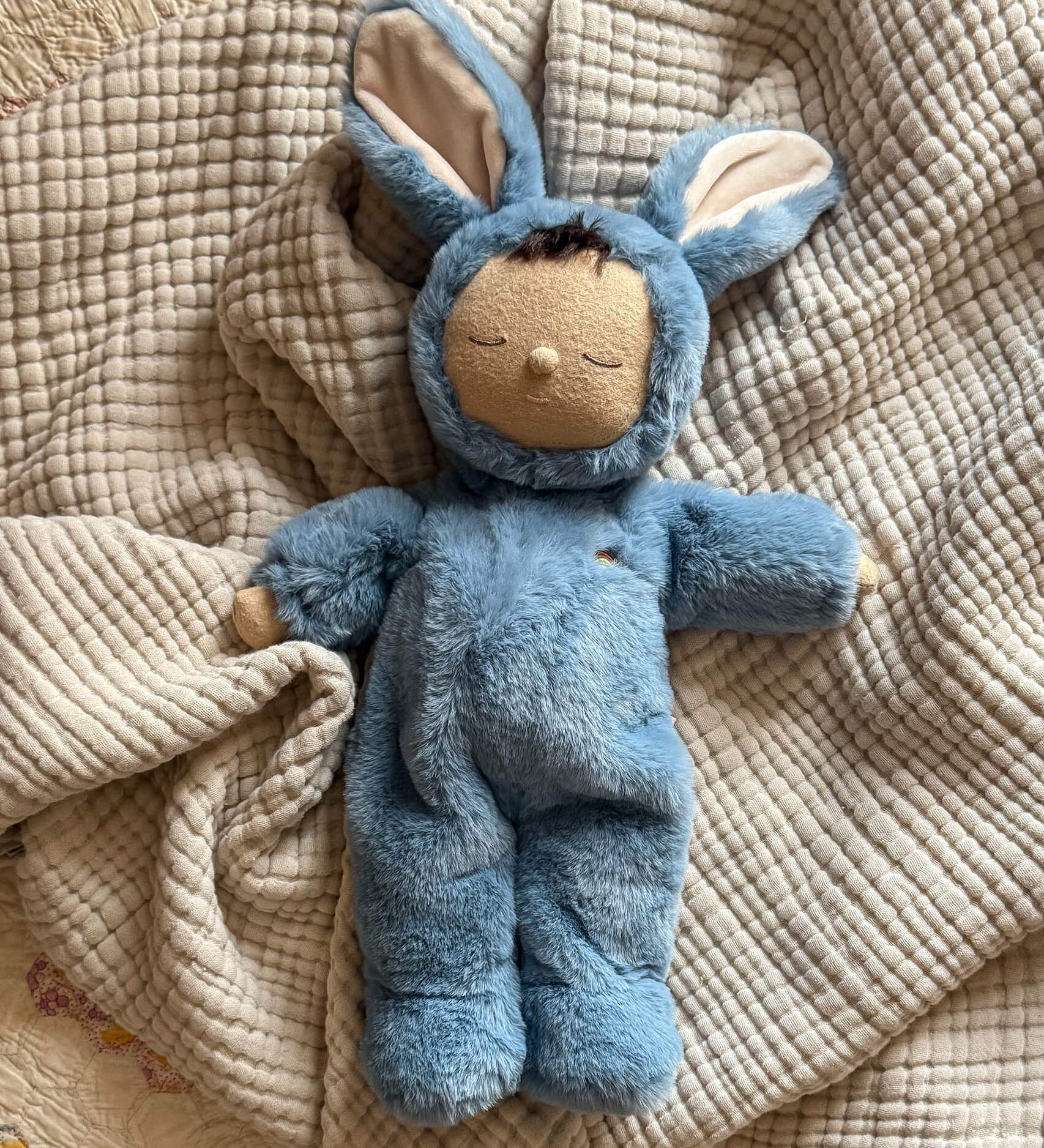 Olli Ella cozy dinkum bunny twiggy doll in blue colour lying on top of a soft blanket. This fluffy toy doll is available at Babipur