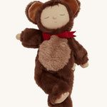 Olli Ella Cozy Dinkums - Teddy Twiggy is a soft body doll, with a soft and fluffy chocolate brown outfit which has a hood and teddy ears on top, and a red bow tie. The image is on a cream background.