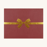 The packaging of the Olli Ella Dinkum Dolls Petal Carrier - Red Velvet. The box is a deep red colour, with a gold bow printed on the front.