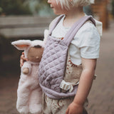 A close up of a child holding a Olli Ella cozy bunny doll whilst wearing the Olli Ella quilted toy carrier in lavender showing the quilted detail. This toy carrier is available at Babipur.
