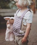 A close up of a child holding a Olli Ella cozy bunny doll whilst wearing the Olli Ella quilted toy carrier in lavender showing the quilted detail. This toy carrier is available at Babipur.