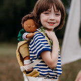 A child carrying a Olli Ella dinkum doll with the Olli Ella toy carrier in honey on their back. This toy carrier is available at Babipur.