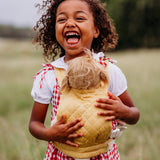 A close up of a child wearing a honey Olli Ella quilted toy carrier with a dinkum doll sitting inside showing the quilted stitch detail. This toy carrier is available at Babipur.