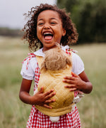 A close up of a child wearing a honey Olli Ella quilted toy carrier with a dinkum doll sitting inside showing the quilted stitch detail. This toy carrier is available at Babipur.