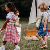 A girl playing and wearing the Olli Ella dinkum doll quilted carrier in  sage colour with a dinkum doll sitting inside on her back. This toy carriers is available at Babipur.