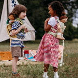 2 Children playing outside and wearing the Olli Ella dinkum doll quilted carriers in sage and honey colours with dinkum dolls sitting inside. These toy carriers are available at Babipur.