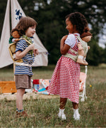 2 Children playing outside and wearing the Olli Ella dinkum doll quilted carriers in sage and honey colours with dinkum dolls sitting inside. These toy carriers are available at Babipur.