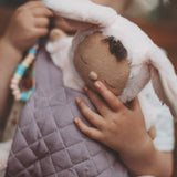 A close up of a child carrying a Olli Ella cozy bunny doll with the Olli Ella toy carrier in lavender showing the quilted stitch detail. This toy carrier is available at Babipur.