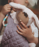 A close up of a child carrying a Olli Ella cozy bunny doll with the Olli Ella toy carrier in lavender showing the quilted stitch detail. This toy carrier is available at Babipur.