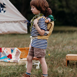 A child walking outside and wearing the Olli Ella dinkum doll quilted carrier in  honey colour with a dinkum doll sitting on it's back. This toy carriers is available at Babipur.