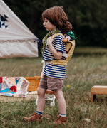 A child walking outside and wearing the Olli Ella dinkum doll quilted carrier in  honey colour with a dinkum doll sitting on it's back. This toy carriers is available at Babipur.