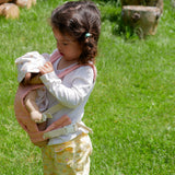 A child playing outside and carrying a Olli Ella dinkum doll with the Olli Ella toy carrier in rose . This toy carrier is available at Babipur.