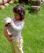 A child playing outside and carrying a Olli Ella dinkum doll with the Olli Ella toy carrier in rose . This toy carrier is available at Babipur.