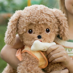 A child holding the soft and fluffy brown Olli Ella Goldie dinkum dog with a magnetic bone in its mouth.