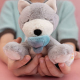 A child holding the soft grey and white Olli Ella dinkum puppy in their hands for scale