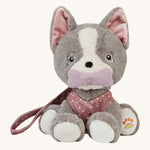 Olli Ella Dinkum Dog - Gizmo is wearing their dark pink with white spotted harness, and is holding their dark pink plush bone in their mouth