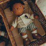 An Olli Ella Dinkum Doll, comfy in an Olli Ella Strolley, lying on the Champagne mattress. The Dinkum Doll wears the Olli Ella Dinkum Doll Holiday Outfit Set, white sock and brown shoes.