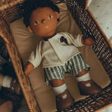 An Olli Ella Dinkum Doll, comfy in an Olli Ella Strolley, lying on the Champagne mattress. The Dinkum Doll wears the Olli Ella Dinkum Doll Holiday Outfit Set, white sock and brown shoes.